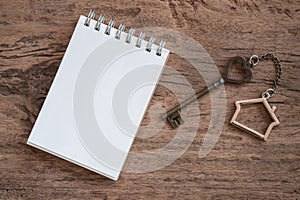 House key with home keyring, blank notebook and pencil on old wood table background