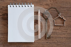 House key with home keyring, blank notebook and pencil on old wood table background