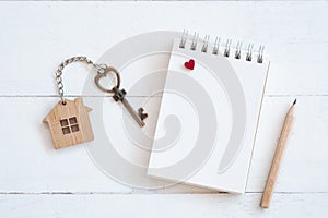 House key with home keyring, blank notebook and pencil on white wood table background