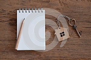 House key with home keyring, blank notebook and pencil on white wood table background