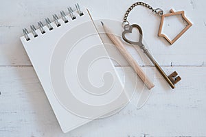 House key with home keyring, blank notebook and pencil on white wood table background