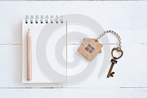 House key with home keyring, blank notebook and pencil on white wood table background