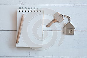 House key with home keyring, blank notebook and pencil on white wood table background