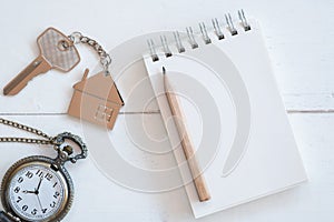 House key with home keyring, blank notebook and pencil on white wood table background