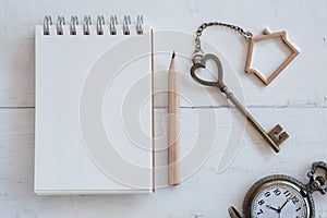 House key with home keyring, blank notebook and pencil on white wood table background