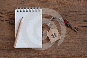 House key with home keyring, blank notebook and pencil on white wood table background