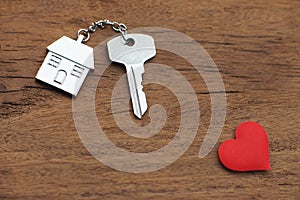 House key with home keyring decorated with mini red heart on wood texture background, sweet home concept