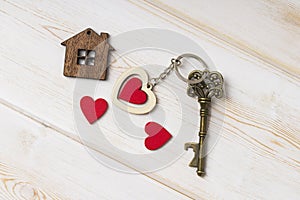 House key with home keyring decorated with wooden  heart.  Old key with a heart on white wood . sweet home concept