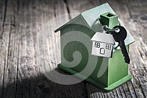 House key on a house shaped keychain with green wooden home environmentally friendly property