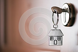 House key on a house shaped silver keyring in the lock of a entrance brown door