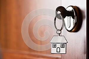 House key on a house shaped silver keyring in the lock of a entrance door