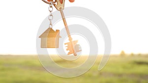 House key with keychain in hand. Background of the sky, sunlight and field. Dream of home, building a cottage in the countryside,