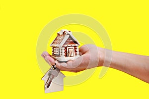 House and key with keychain in your hand on yellow background, selling buying or renting an apartment