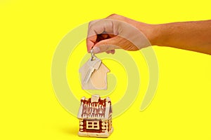 House and key with keychain in your hand on yellow background, selling buying or renting an apartment