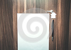 House and key with a pen and blank paper on the wood background.