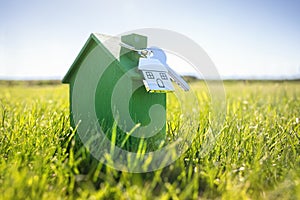 House key on a house shaped keychain with green wooden eco home on grass