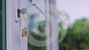 The house key for unlocking a new house is plugged into the white door. The keychain is moving after the wind blows. house for sel