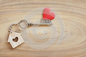 House keyring and love shape key on vintage wooden table. Decorated with mini heart as sweet gift for lover or family member. Home