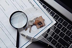 House keys, magnifying glass, and contract on a laptop. Concept of rent, search, purchase real estate