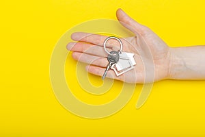 House keys with trinket in female hand on color background, top view with copy space. House key on yellow background. Minimal flat