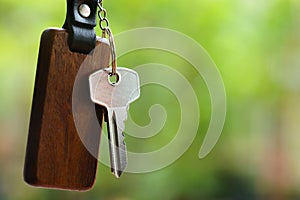 House keys with wooden home keyring with green garden background, property concept, copy space