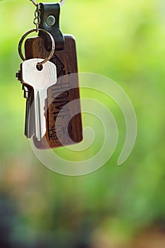 House keys with wooden home keyring with green garden background, property concept, copy space