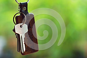 House keys with wooden home keyring with green garden background, property concept, copy space