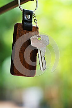 House keys with wooden home keyring with green garden background, property concept, copy space