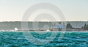 House and lighthouse on island with ocean waves crashing on shoreline