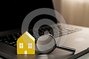 House and magnifying glass on laptop keyboard.