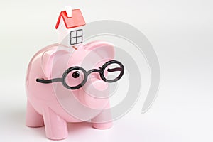 House maintenance budget, cost, savings or mortgage home loan concept, miniature house on pink piggy bank wearing glasses on white