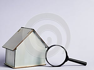 House miniature with magnifying glass against white background. Property inspection or investment.