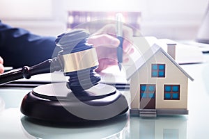 House Model With Gavel In Front Of A Businessperson