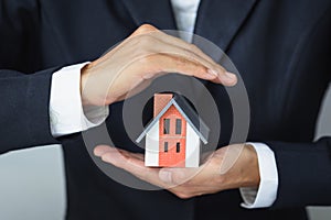 A house model in the hands of a businessman To protect home protection concept using real estate investor`s gestures and symbols,