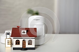 House model, lock, smoke and movement detectors on table in room, space for text. Home security system