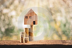 House model put on the stack gold coin with growing interest value on sunlight in the public park.