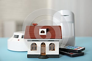 House model, remote controls, smoke and movement detectors on light blue table in room. Home security system photo