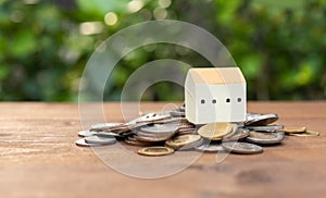 House model set on money coins pile over wood table with nature background