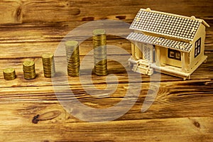 House model and stacks of golden coins on wooden background. Property investment, home loan, house mortgage, real estate concept