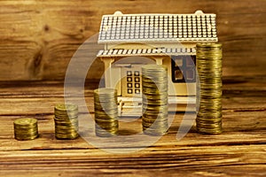 House model and stacks of golden coins on wooden background. Property investment, home loan, house mortgage, real estate concept