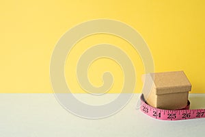 House model and tape measure on gray and yellow background. Real estate concept