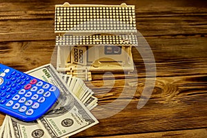 House model, U.S. one hundred dollar bills and calculator on wooden background. Property investment, home loan, house mortgage