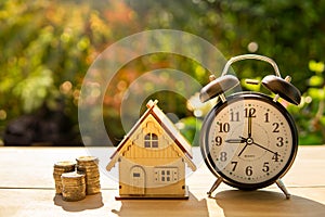 The house money coins and alarm clock stack on wood table and sunset background in the public pack and Business concept.