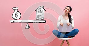 House and money on the scale with woman using a laptop