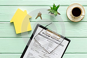 House mortgage with application, glasses, coffee, house toy, keys on mint green wooden banker desk background top view