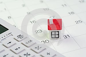 House mortgage payment and installment schedule concept, small miniature house on end of month calendar with calculator photo