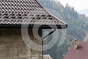 House with new brown metal tile roof and rain gutter. Metallic Guttering System, Guttering and Drainage Pipe Exterior