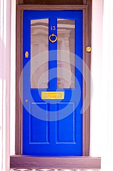 House number 13 on a blue wooden front door with glass seen with door step