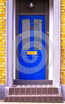 House number 13 on a blue wooden front door with glass seen with door steps leading up