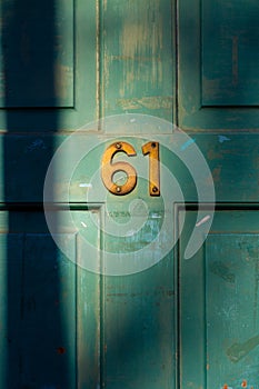 House number 61 on a weathered green wooden front door